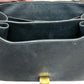 Close-up of the interior of a black pebbled leather handbag, showing the open compartments and a small gold-tone clasp at the bottom.