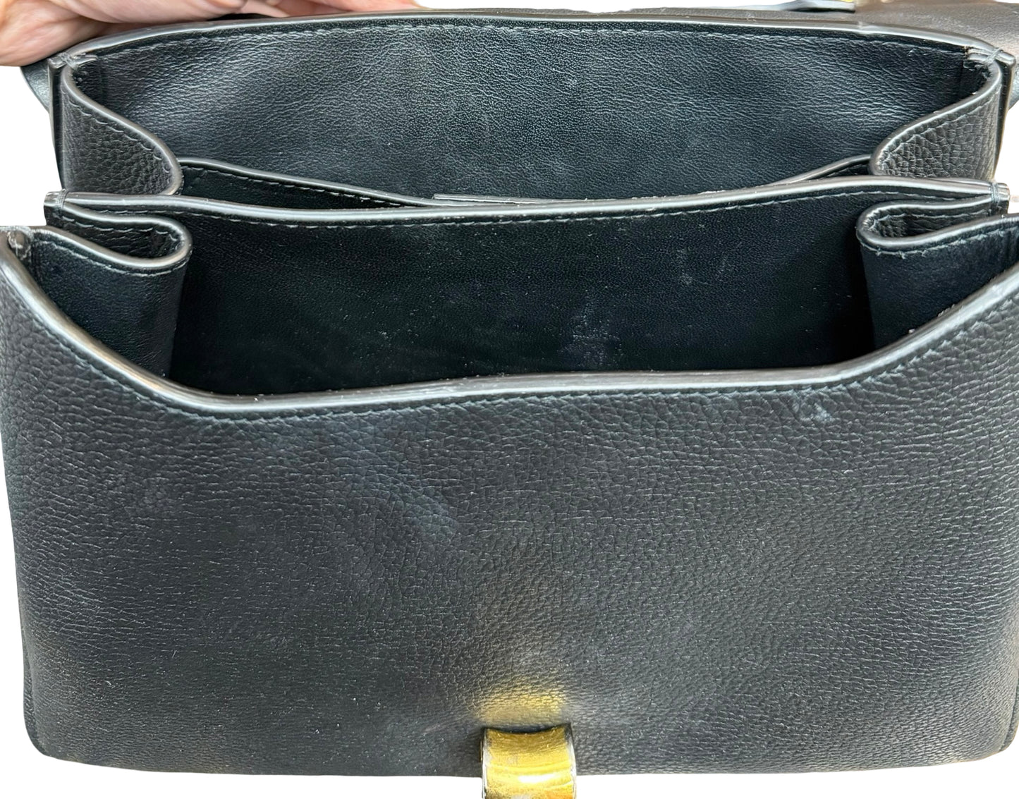 Close-up of the interior of a black pebbled leather handbag, showing the open compartments and a small gold-tone clasp at the bottom.
