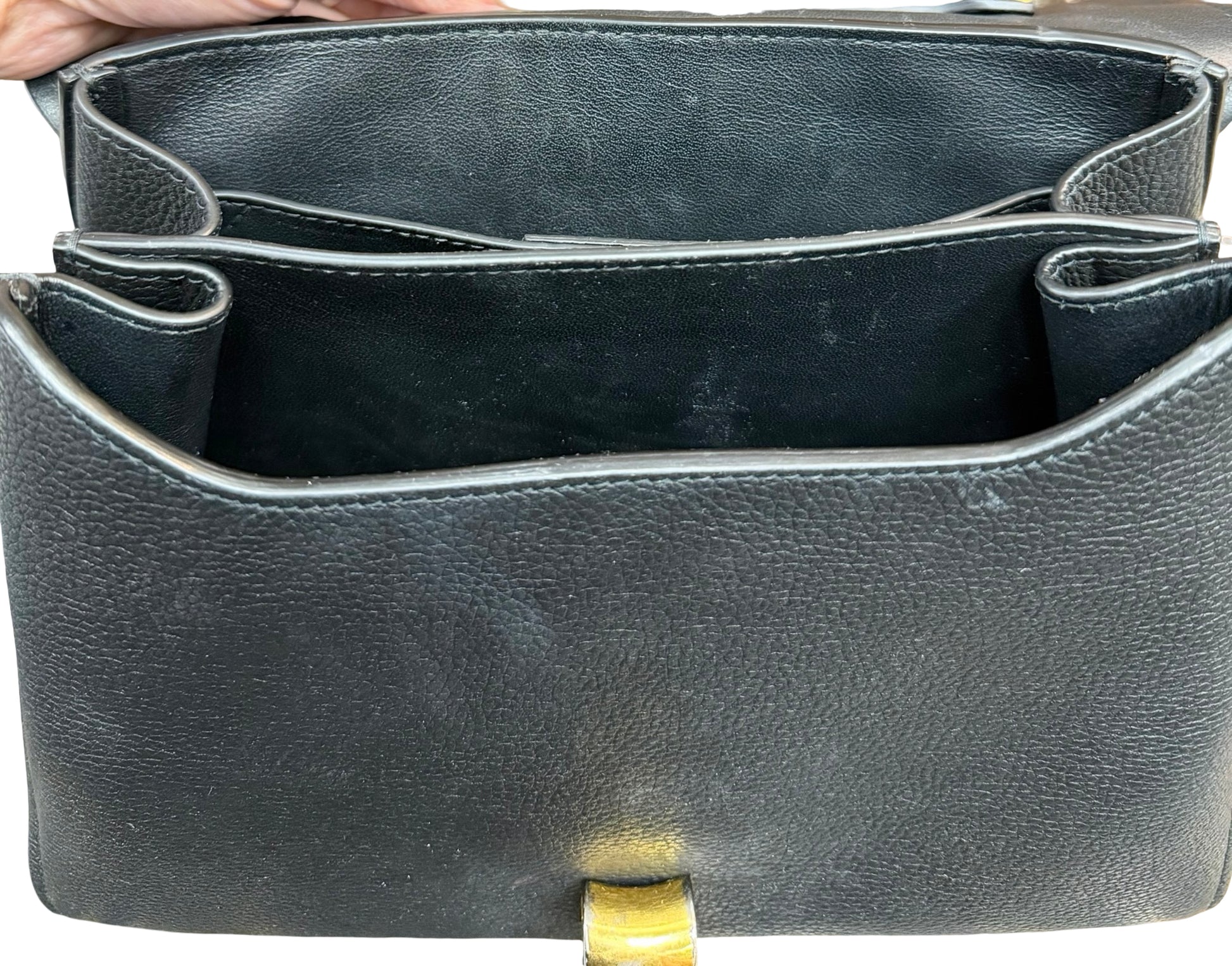 Close-up of the interior of a black pebbled leather handbag, showing the open compartments and a small gold-tone clasp at the bottom.