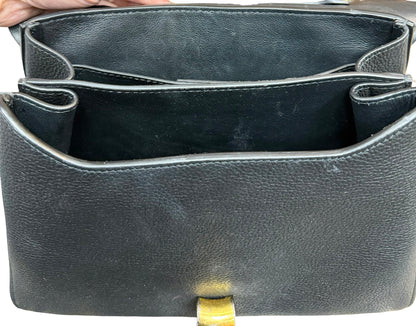 Close-up of the interior of a black pebbled leather handbag, showing the open compartments and a small gold-tone clasp at the bottom.