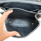 Close-up of a black leather handbag interior with a hand holding the opening to show the spacious compartment and gold-tone hardware.