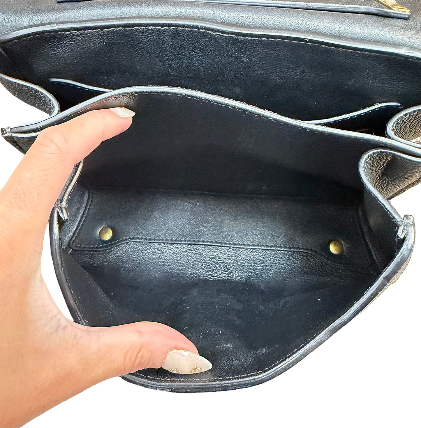 Close-up of a black leather handbag interior with a hand holding the opening to show the spacious compartment and gold-tone hardware.