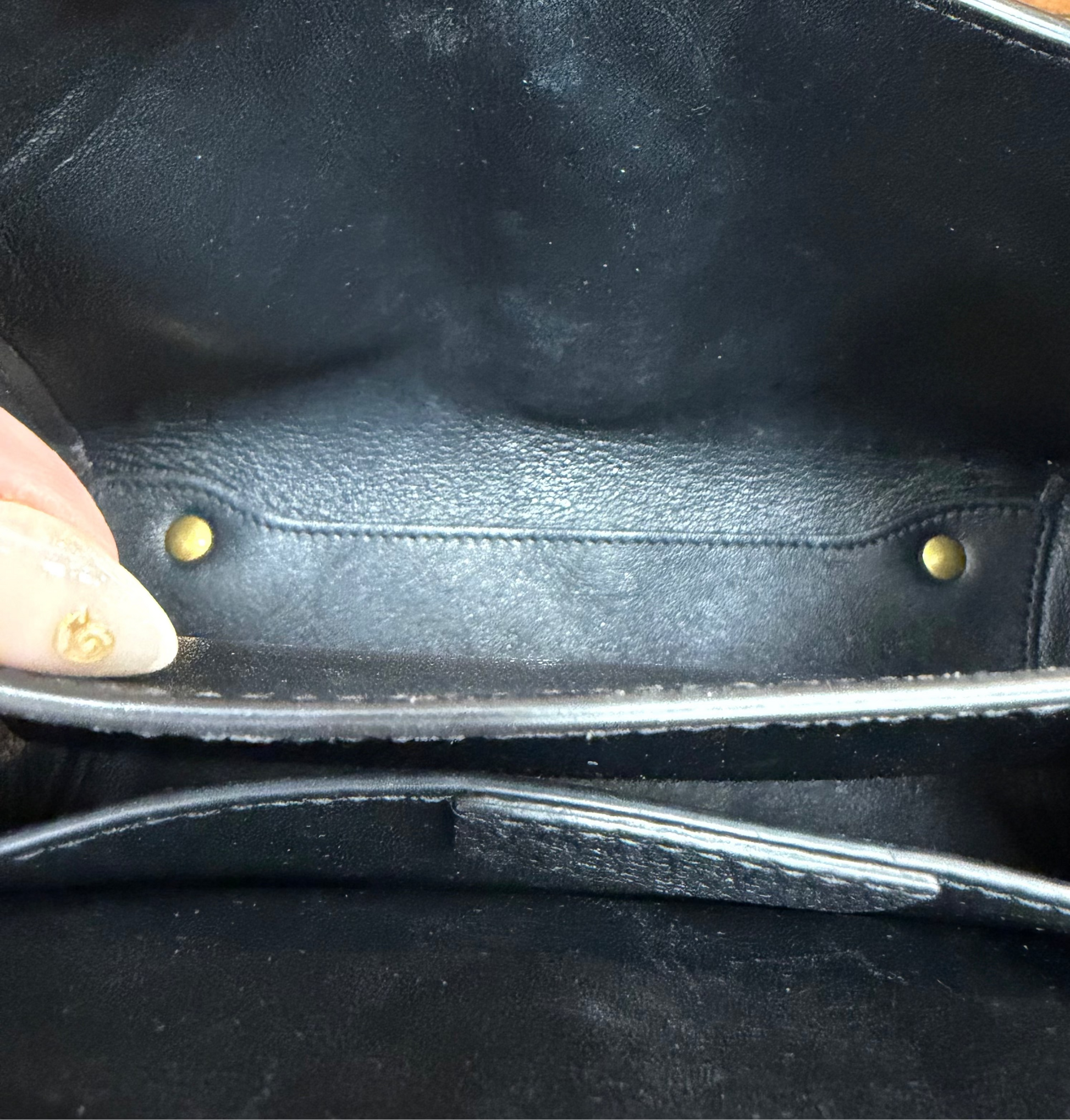Close-up of the interior of a black leather handbag, showing the lining, and gold-tone hardware.