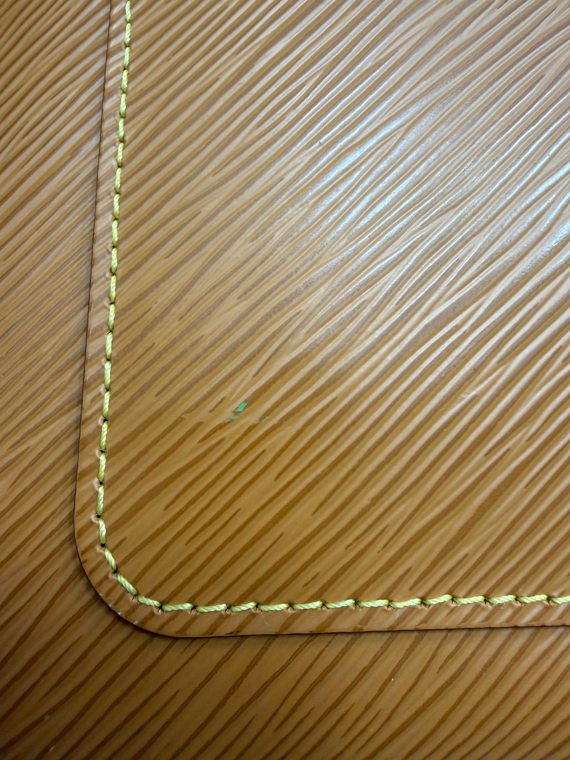Close-up of a brown textured leather corner with light yellow stitching with a small light green-colored stain