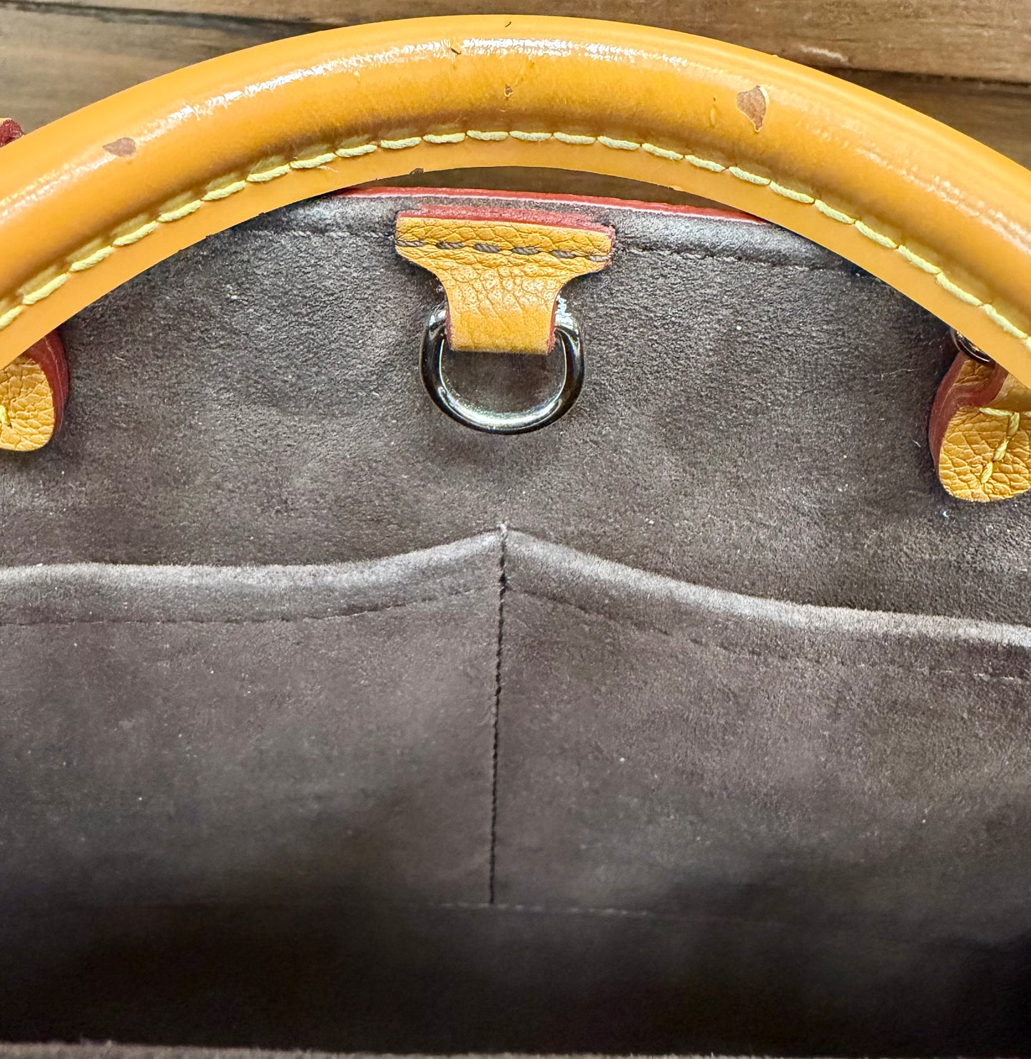 Close-up of a handbag's interior showing a brown leather handle, silver hardware, and a dark brown lining. The handle shows ships in the leather