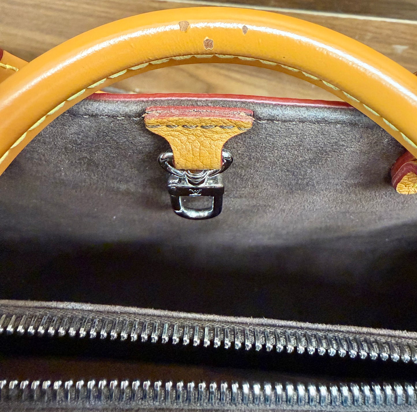 Close-up of handbag showing the interior lining, silver zipper, and a brown leather handle with chips in the leather