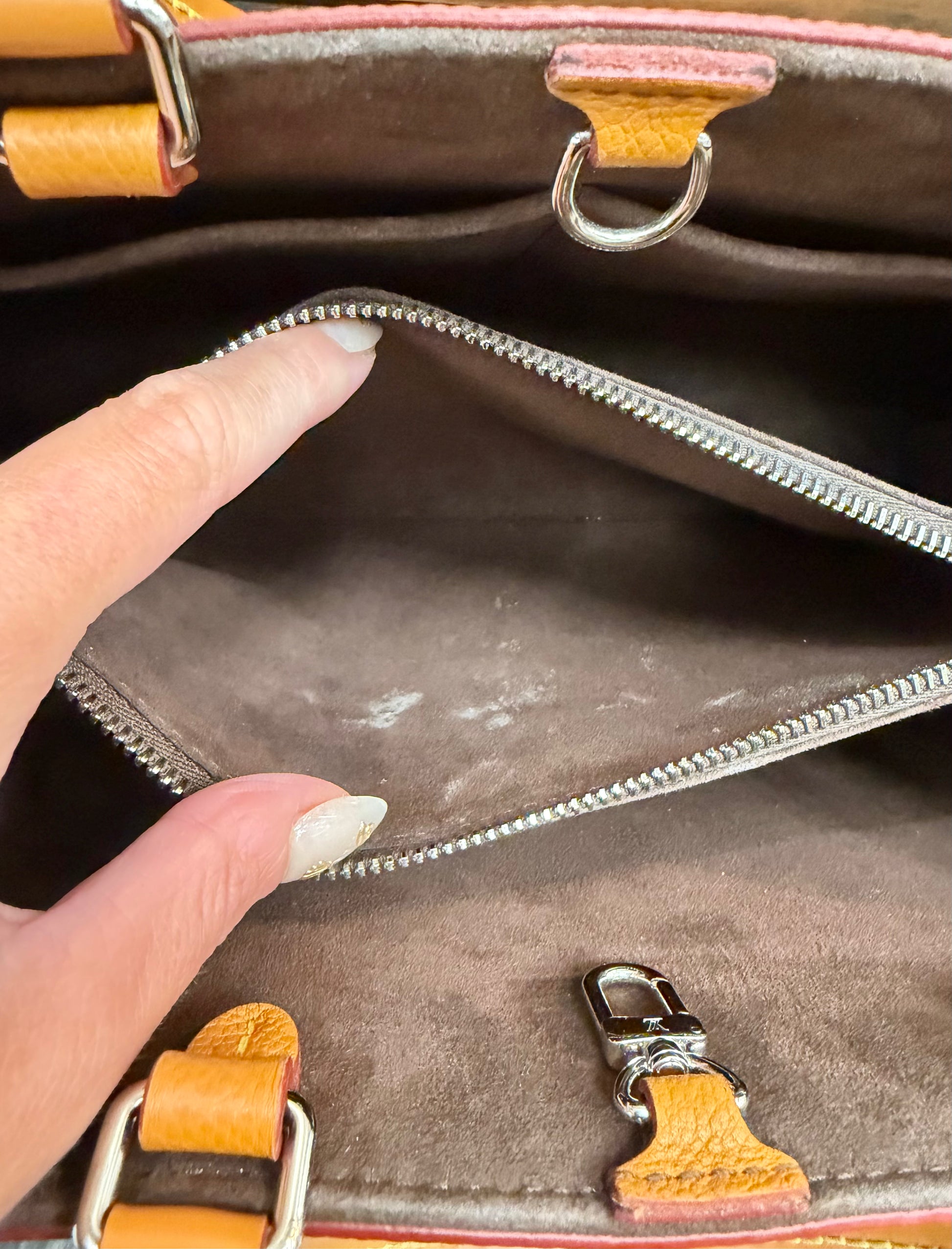 Close-up of the interior of a brown handbag, showing a zippered compartment opened by a person's fingers, with brown trim. There are white stains in the brown zipper compartment.