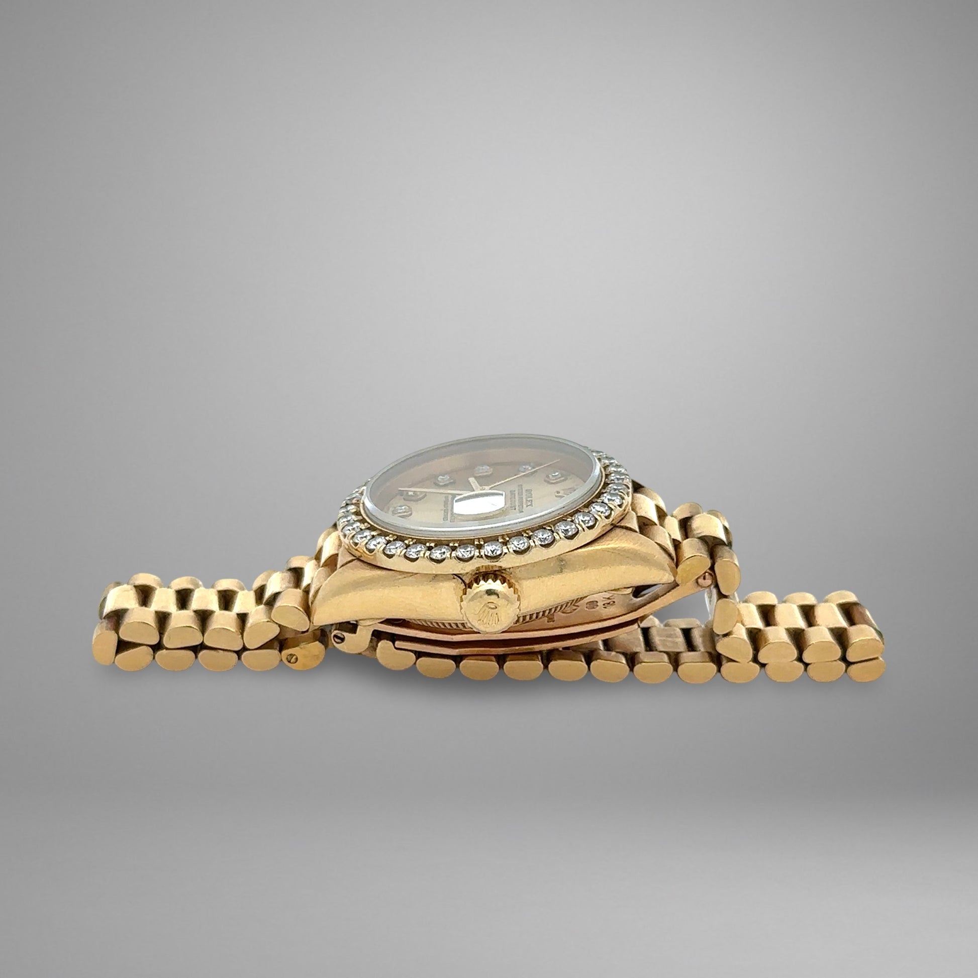 Gold wristwatch with diamond-studded bezel on a gray background
