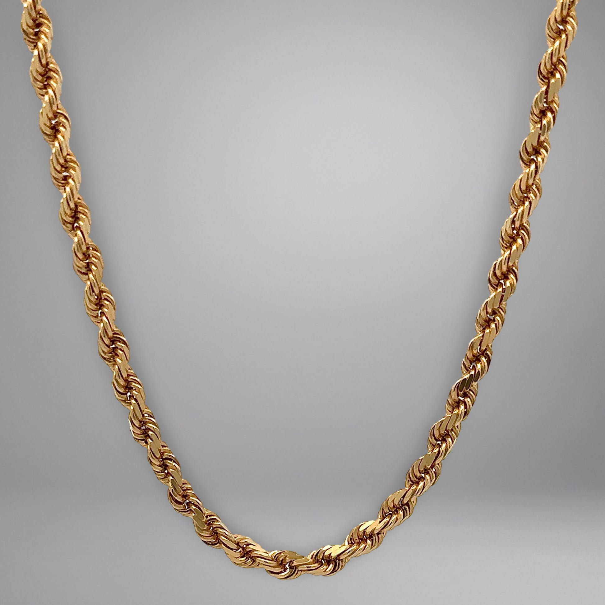 Gold rope chain necklace on a gray background