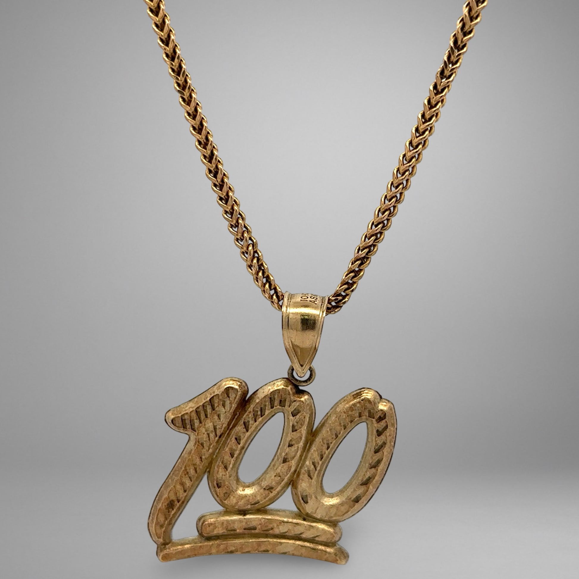 Gold necklace with a '100' pendant on a gray background