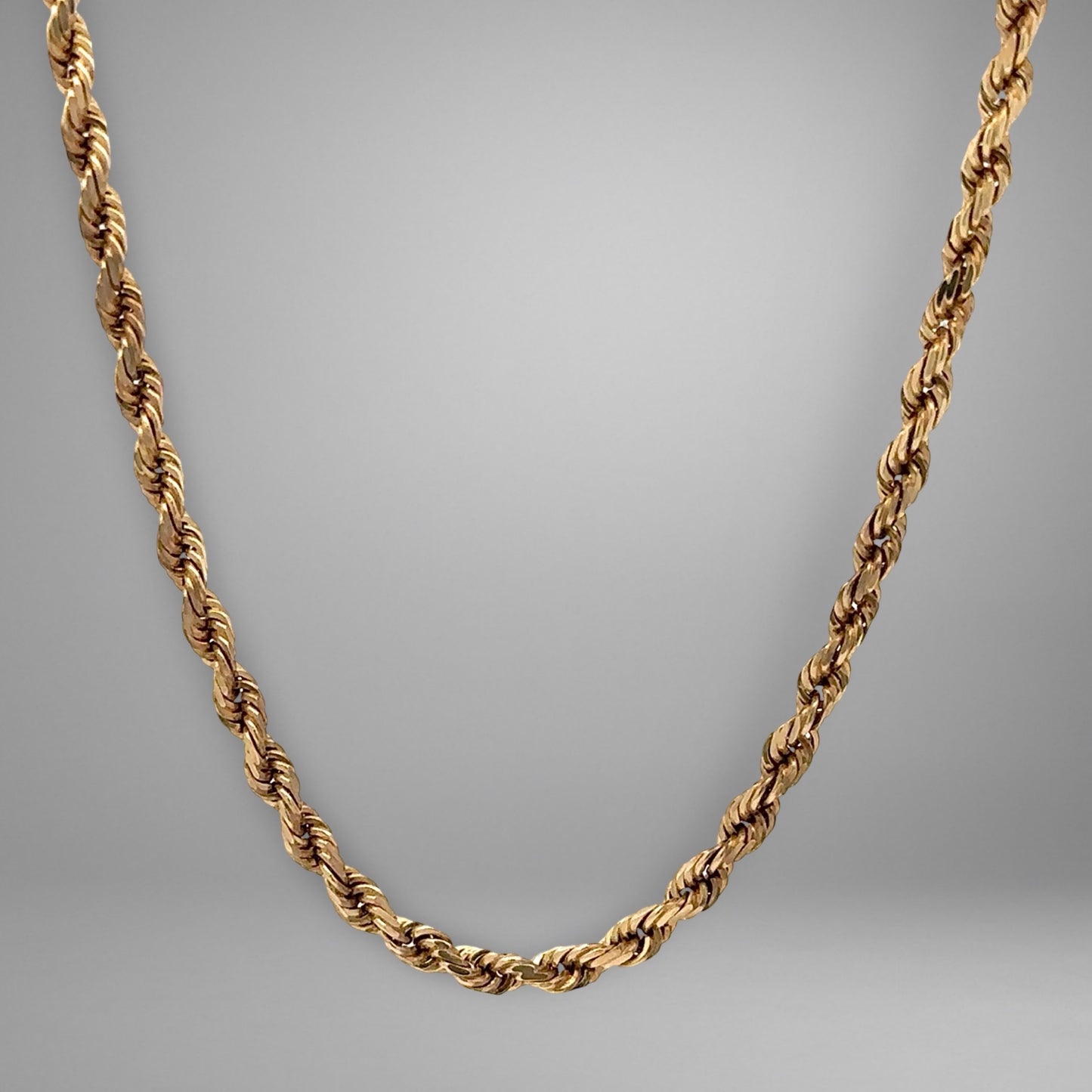 Gold rope chain necklace on a gray background