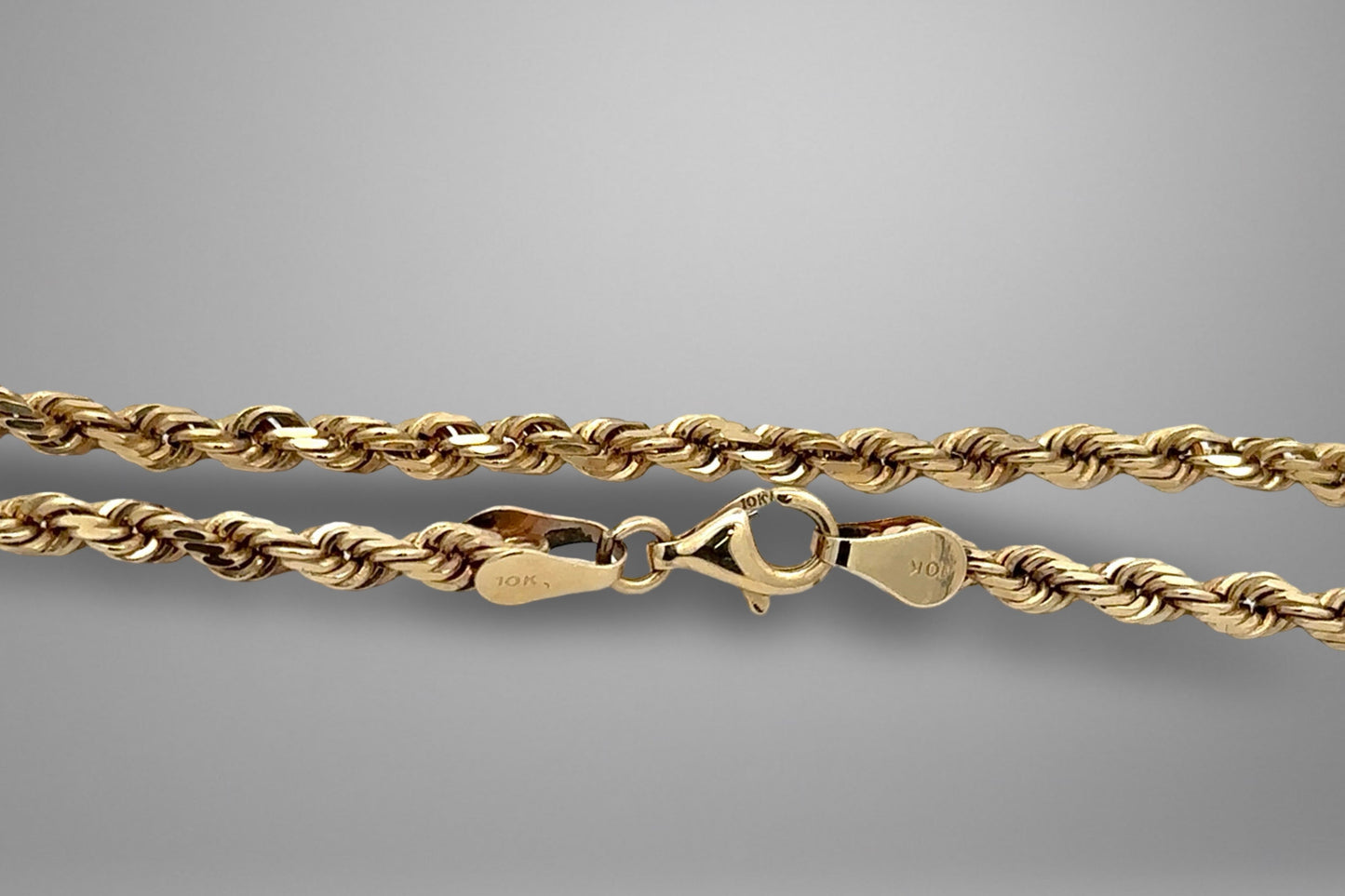 Gold rope chain necklace on a gray background