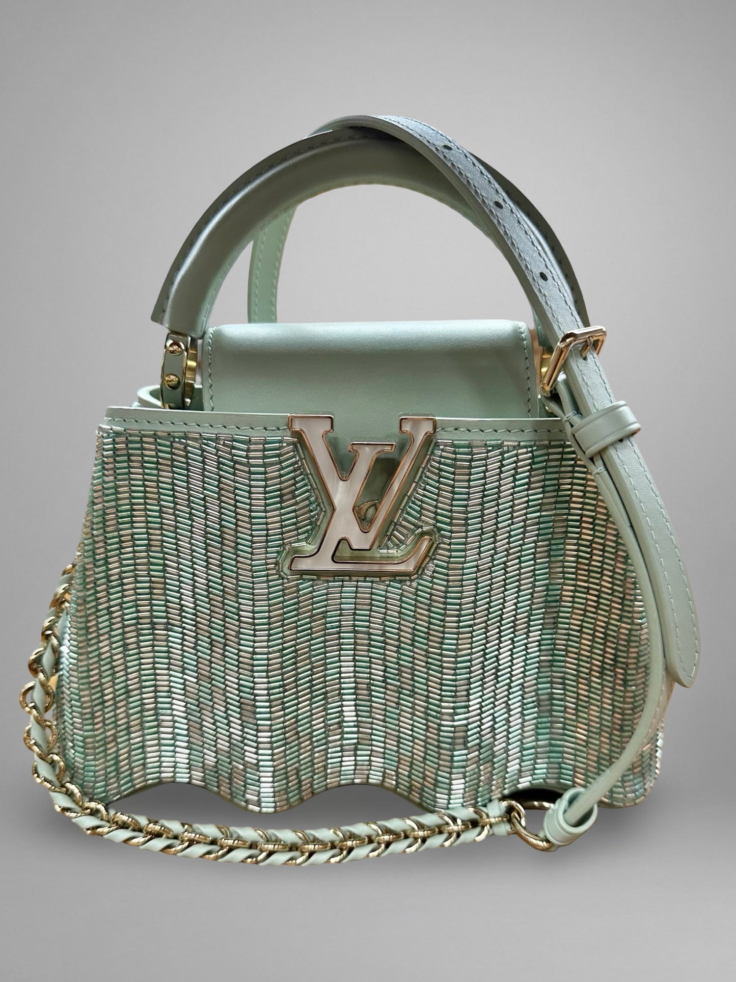 Light blue handbag with chain detail and visible brand logo on a gray background