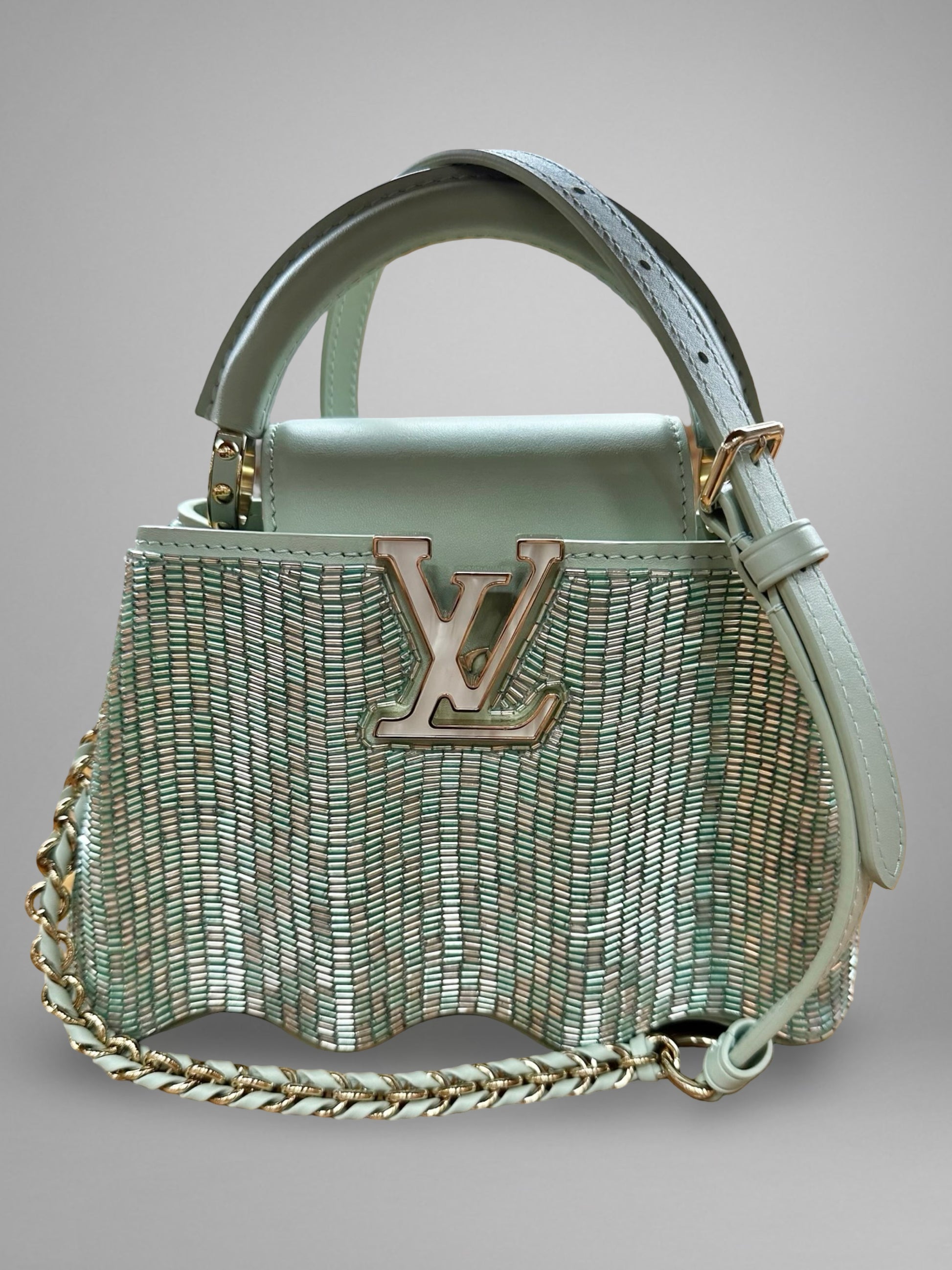 Light blue handbag with chain detail and visible brand logo on a gray background