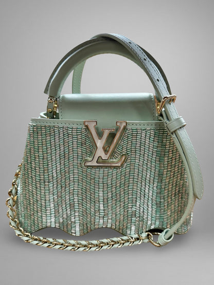 Light blue handbag with chain detail and visible brand logo on a gray background