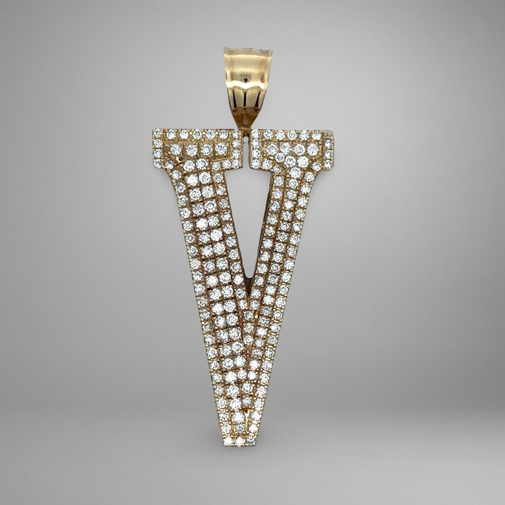 Gold and diamond-studded letter 'V' pendant on a gray background