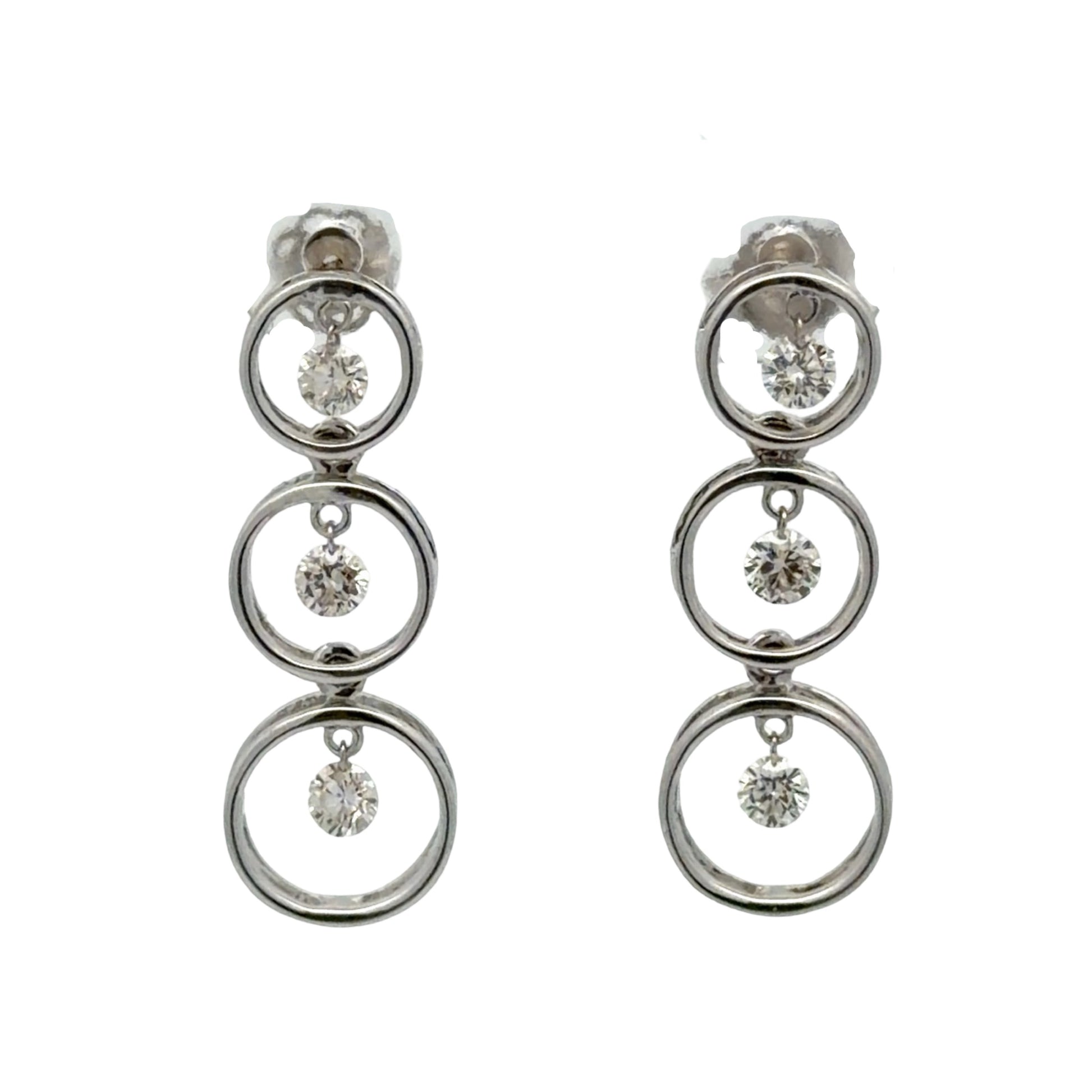 Pair of white gold earrings with multiple circular designs on a white background and floating diamonds inside each circle