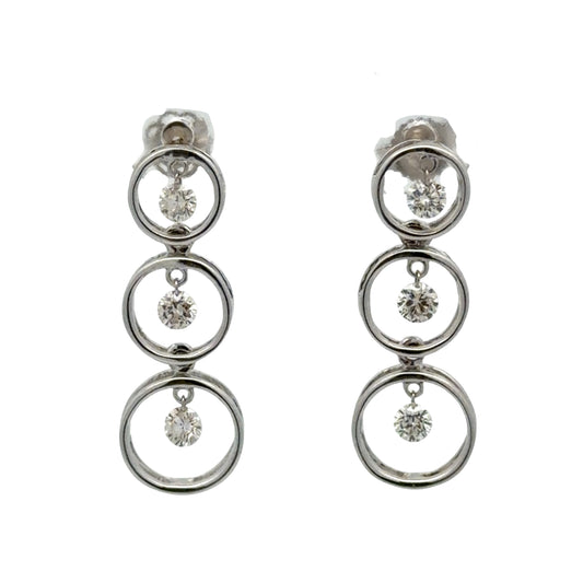 Pair of white gold earrings with multiple circular designs on a white background and floating diamonds inside each circle