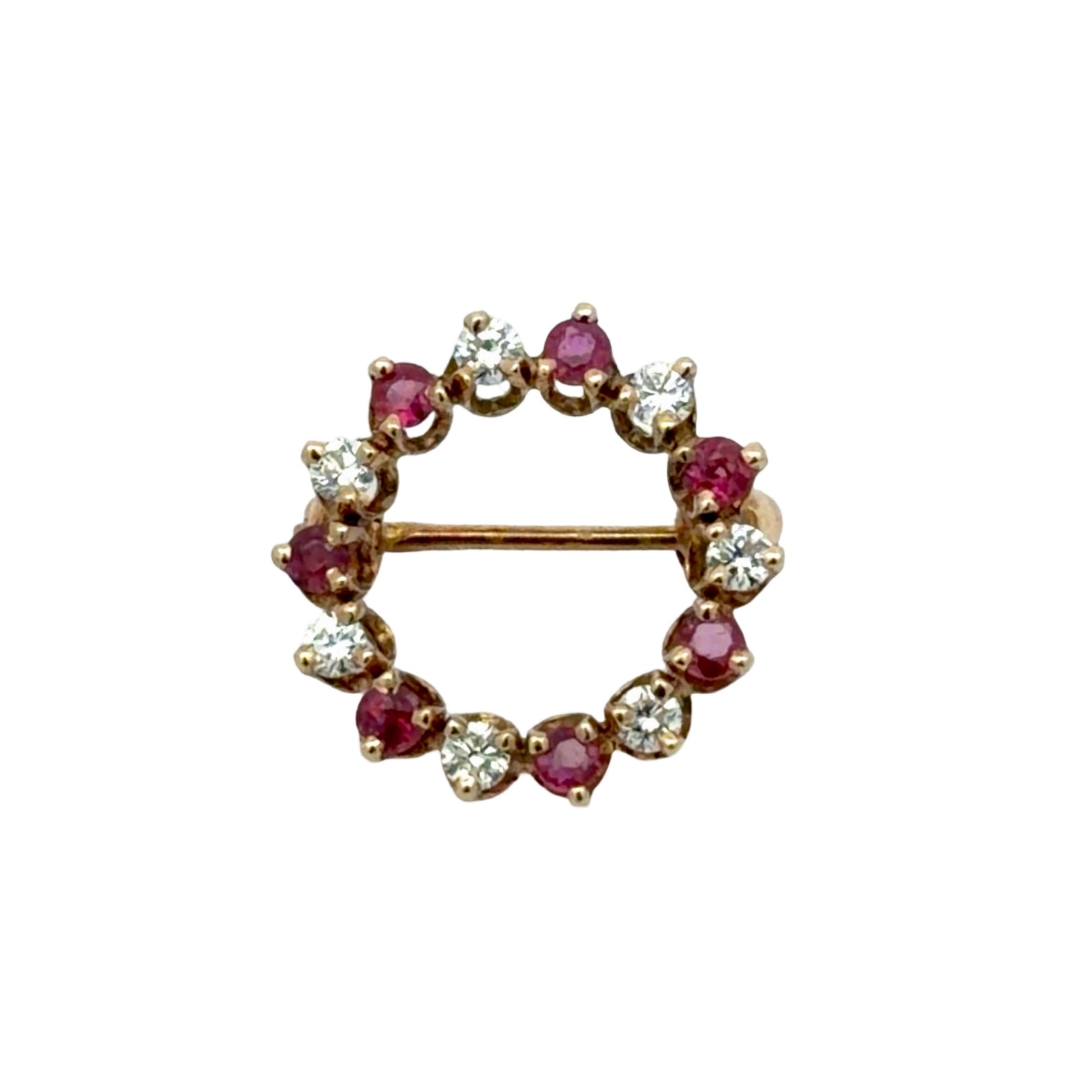 Circular brooch with round diamonds and red gemstones on a white background