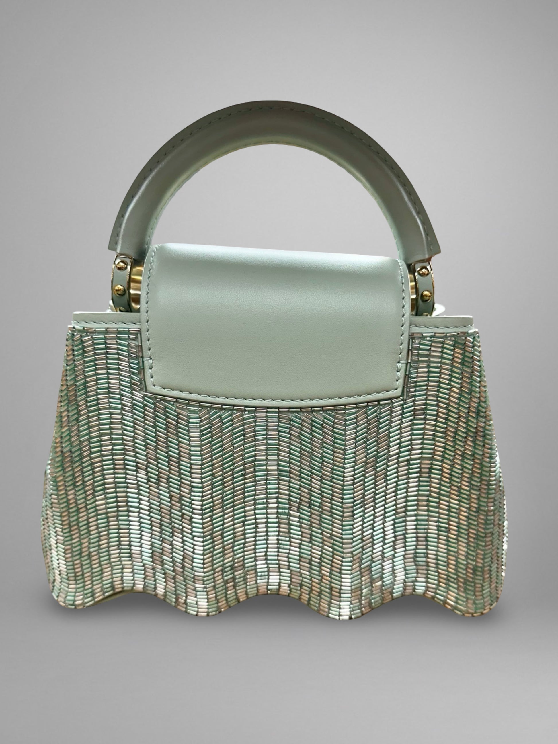 Light green handbag with metallic handle on a gray background