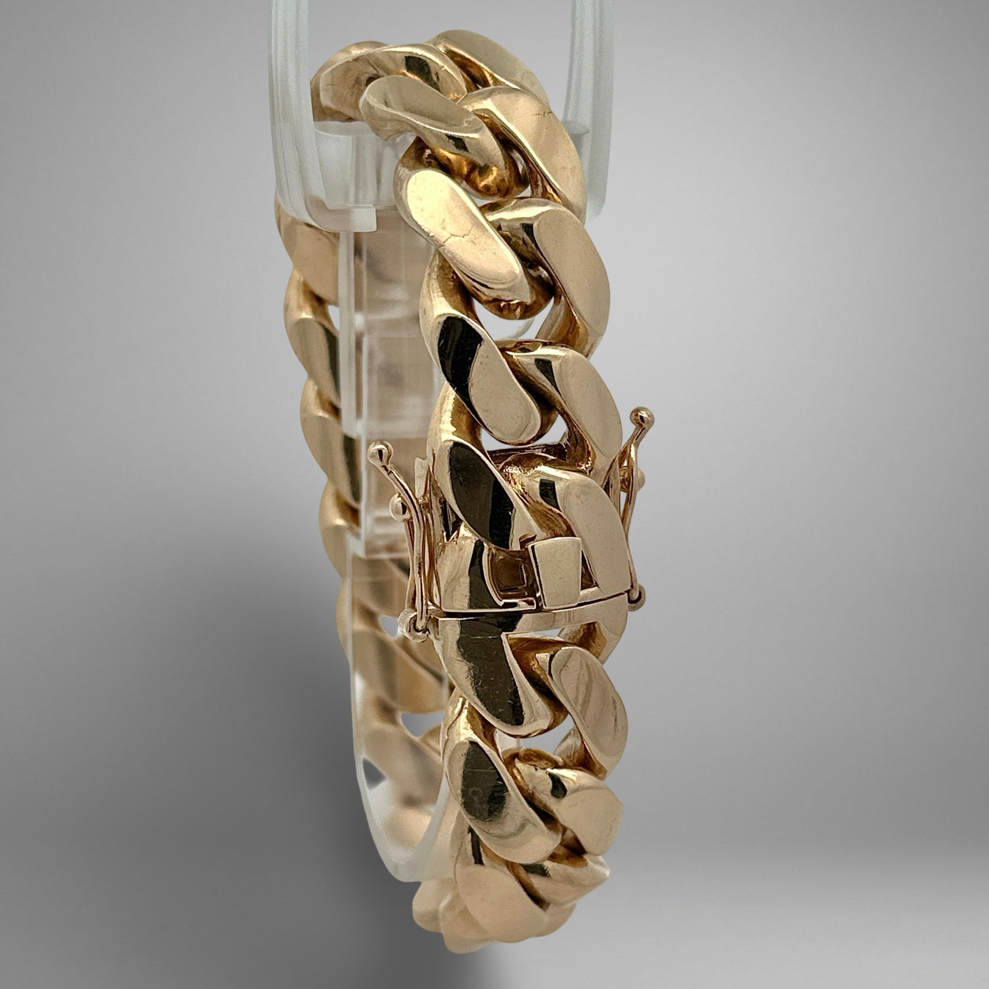 Gold bracelet on a clear stand against a gray background