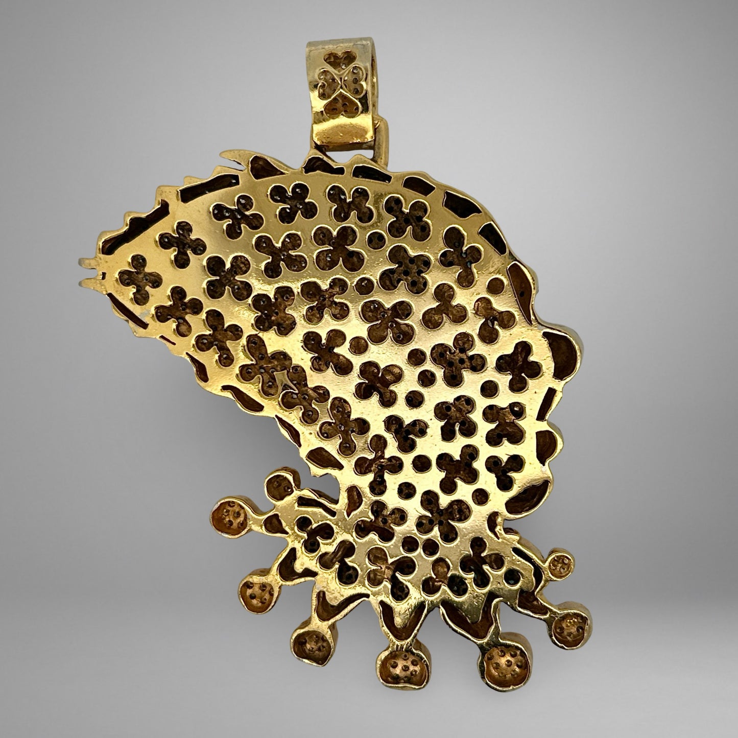 Back of gold pendant with intricate floral design on a gray background