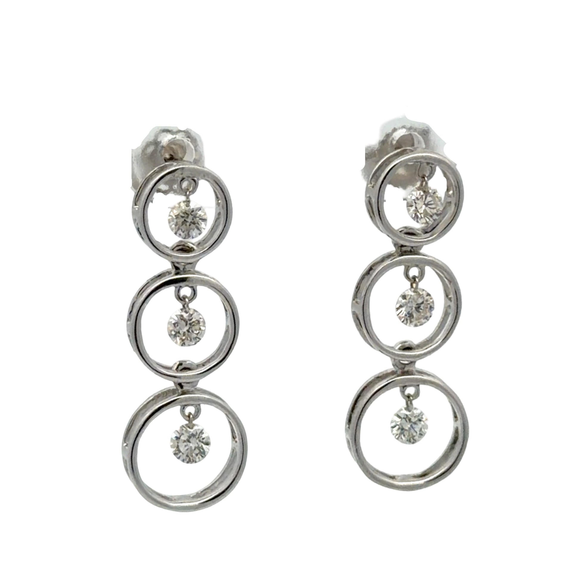 Pair of white gold earrings with multiple circular designs on a white background with floating diamonds in each circle