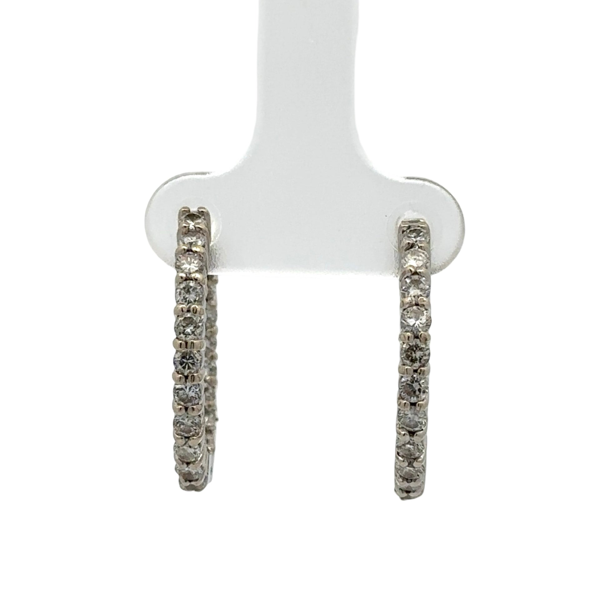 Pair of diamond hoop earrings on a white stand against a white background