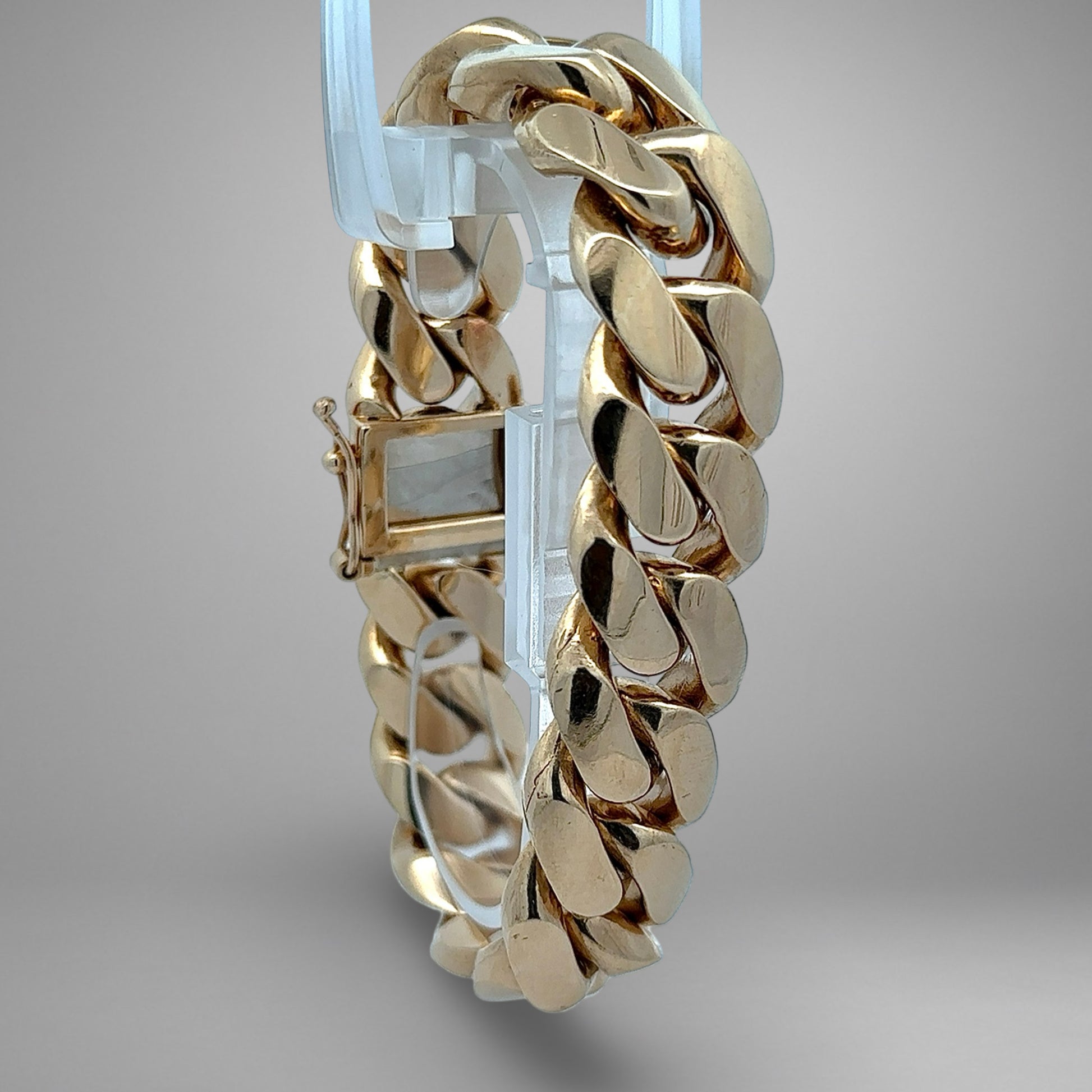 Gold bracelet on a clear stand against a gray background