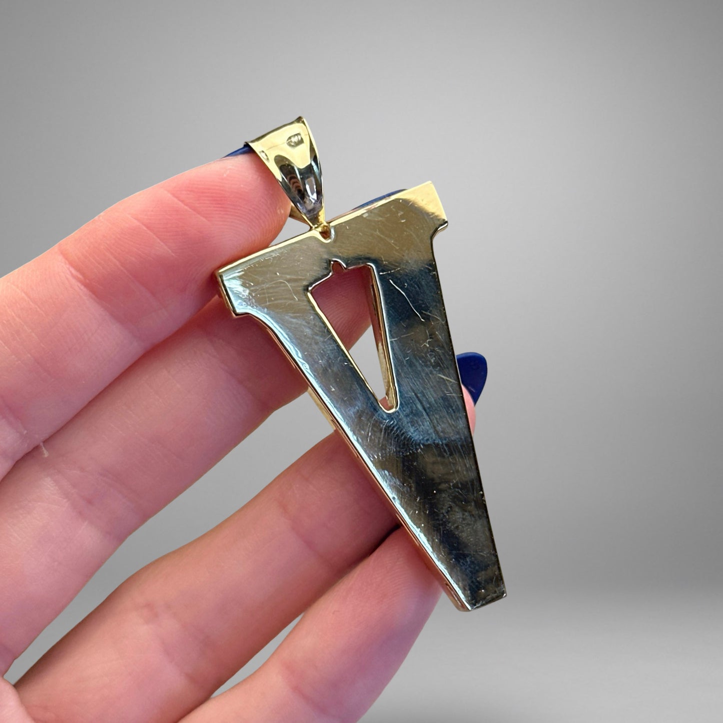 Gold 'V' shaped pendant held by a hand against a gray background